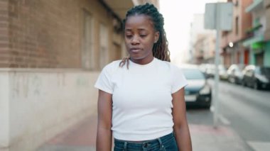 Afro-Amerikalı kadın gülümsüyor. Kollarını kavuşturup caddede duruyor.