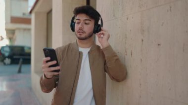 Genç İspanyol adam, kendine güvenen, sokakta akıllı telefon kullanan, müzik dinleyen.