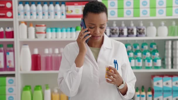 Αφροαμερικανή Φαρμακοποιός Κρατώντας Χάπια Μπουκάλι Μιλάμε Στο Smartphone Στο Φαρμακείο — Αρχείο Βίντεο
