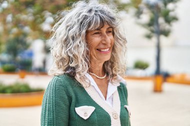 Orta yaşlı bir kadın parkta kendine güvenerek gülümsüyor.