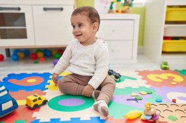 Tapılası İspanyol çocuk anaokulunda yerde kendinden emin bir şekilde otururken gülümsüyor.