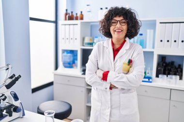 Genç ve güzel İspanyol bilim kadını gülümsüyor. Kollarını kavuşturup laboratuvarda kendine güveniyor.