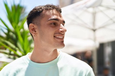 Young hispanic man smiling confident looking to the side at street