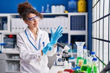 Young hispanic woman scientist smiling confident wearing gloves at laboratory