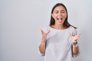 Young hispanic woman standing over white background celebrating mad and crazy for success with arms raised and closed eyes screaming excited. winner concept 