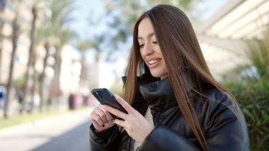 Parkta akıllı telefon kullanarak gülümseyen güzel bir İspanyol kadın.