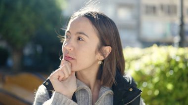 Young beautiful hispanic woman standing with doubt expression at park