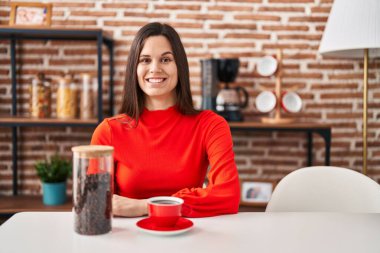 Young hispanic woman drinking coffee at home looking positive and happy standing and smiling with a confident smile showing teeth 