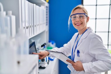 Young blonde woman scientist using computer reading document at laboratory