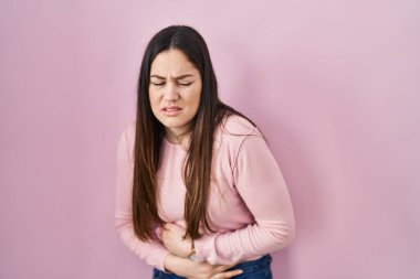 Genç esmer kadın, elleri karnında pembe arka planda duruyor çünkü hazımsızlık, acı verici bir hastalık kendini iyi hissetmiyor. Ağrı kavramı. 