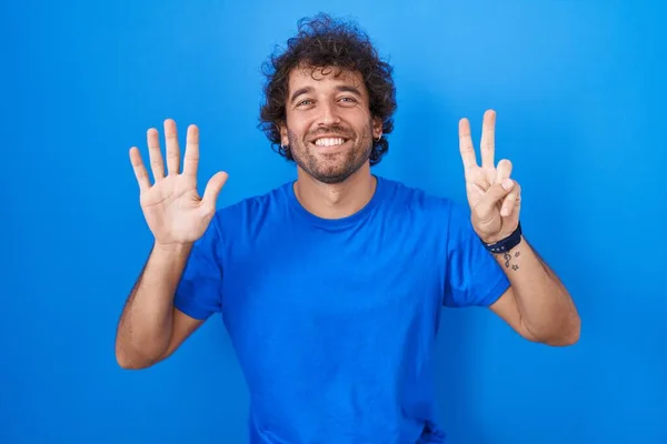 西班牙裔年轻人站在蓝色的背景上 用七号手指指指着 面带微笑 自信而快乐 — 图库照片
