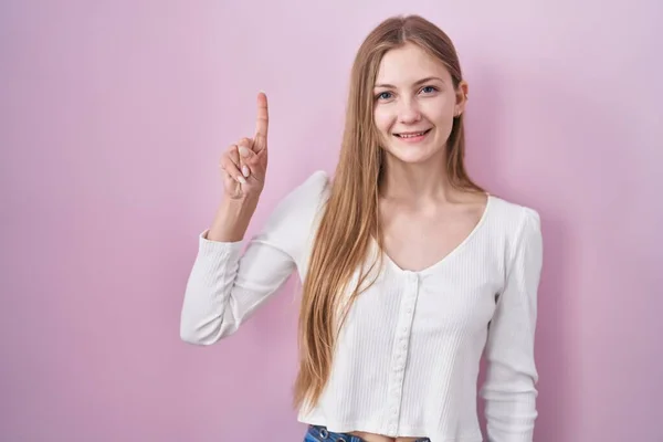 年轻的高加索女人站在粉红的背景上 带着第一指尖 面带微笑 自信而快乐 — 图库照片
