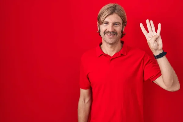白种人留着胡子 站在红色的背景上 用四号手指指指着 面带微笑 自信而快乐 — 图库照片