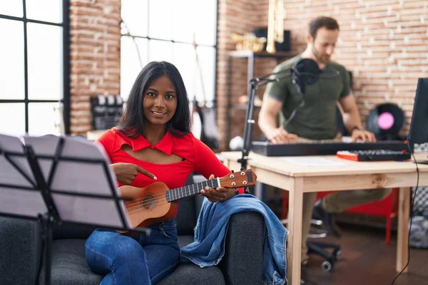 Young indian woman playing ukulele at music studio smiling happy pointing with hand and finger