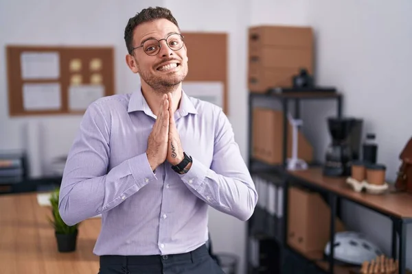 Young Hispanic Man Office Praying Hands Together Asking Forgiveness Smiling — Stockfoto