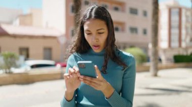 Young african american woman smiling confident using smartphone at street