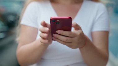 Sokakta akıllı telefon kullanan genç sarışın kadın.