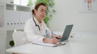 Middle age woman wearing doctor uniform using laptop at clinic