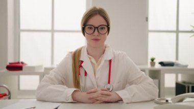 Klinikte doktor üniforması giyen genç sarışın kadın konuşuyor.