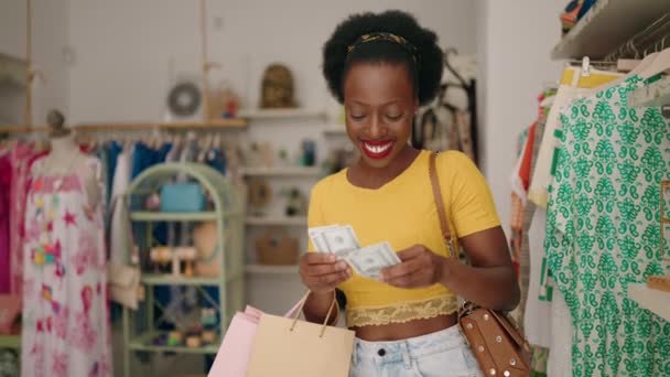 アフリカ系アメリカ人女性の顧客は衣料品店でドルを数えるショッピングバッグを保持 — ストック動画