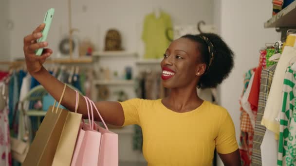 アフリカ系アメリカ人女性の買い物袋を持っている顧客は 衣料品店でスマートフォンでセルフィーを作る — ストック動画