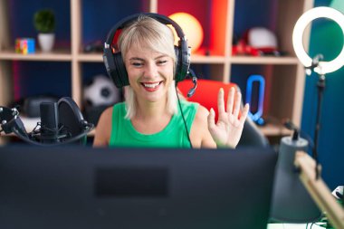 Young caucasian woman playing video games wearing headphones looking positive and happy standing and smiling with a confident smile showing teeth 
