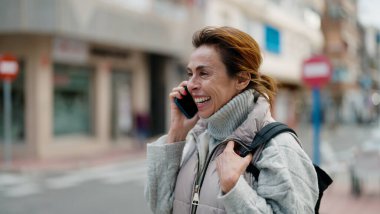 Orta yaşlı İspanyol kadın gülümsüyor. Akıllı telefondan konuşuyor.
