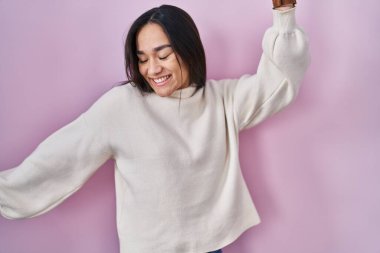 Young south asian woman standing over pink background dancing happy and cheerful, smiling moving casual and confident listening to music 