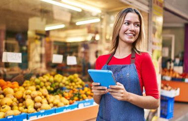 Young hispanic woman shop assistant using touchpad at fruit market