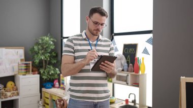 Young caucasian man working as teacher with tablet at kindergarten