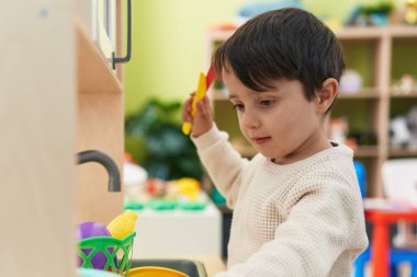 Adorable hispanic boy playing with play kitchen standing at kindergarten