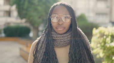 African woman standing with serious expression wearing glasses at park