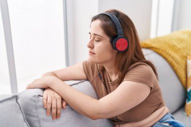 Evdeki kanepede oturmuş müzik dinleyen genç bir kadın.