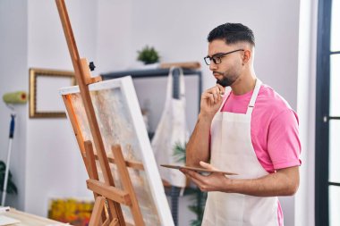 Sanat stüdyosunda çizim yapan genç bir Arap sanatçı şüpheli bir ifadeyle görünüyor.