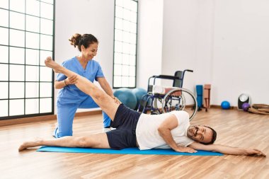 Orta yaşlı bir adam ve kadın fizyoterapi kliniğinde rehabilitasyon seansı yaparken gülümsüyor.