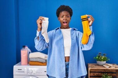 African american woman holding clean andy dirty socks angry and mad screaming frustrated and furious, shouting with anger. rage and aggressive concept. 