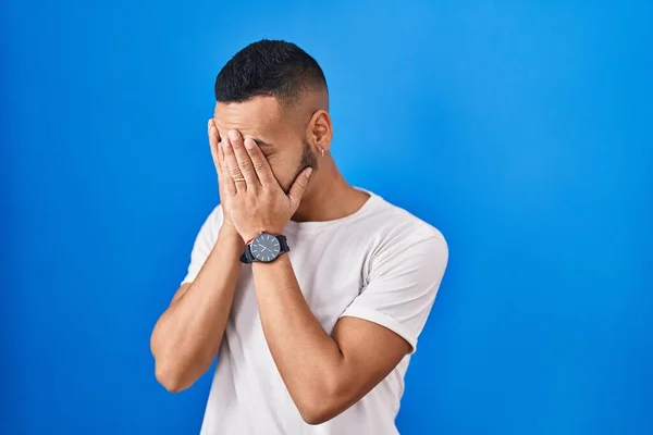 Mladý Hispánec Stojící Nad Modrým Pozadím Smutným Výrazem Zakrývajícím Tvář — Stock fotografie