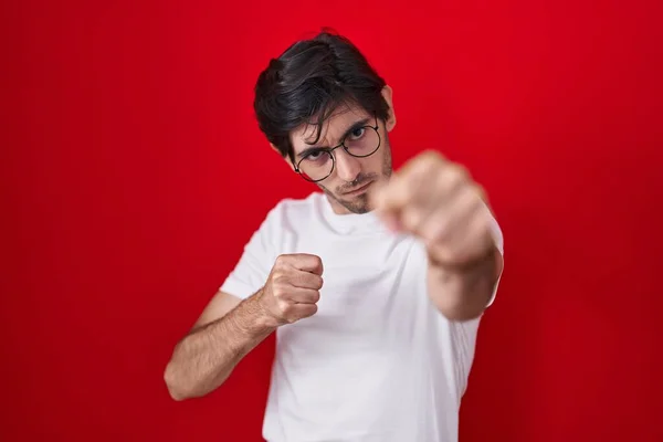 赤の背景に立っている若いヒスパニック系の男が戦うために拳をパンチ 積極的かつ怒りの攻撃 脅威と暴力 — ストック写真