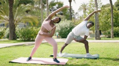 African american man and woman couple smiling confident doing yoga exercise at park