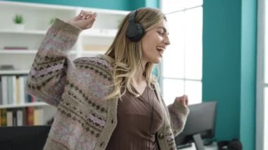 Young blonde woman student listening to music and dancing at library university