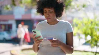 Young african american woman using smartphone and credit card at park