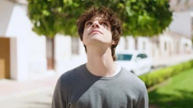 Young hispanic man looking to the sky with relaxed expression at street