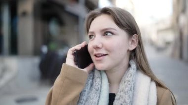 Genç sarışın kadın gülümsüyor. Kendine güveni tam. Akıllı telefondan konuşuyor.