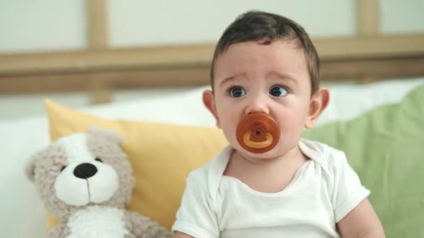 可爱的他的恐慌婴儿吸吮奶嘴坐在床上卧室里 — 图库视频影像