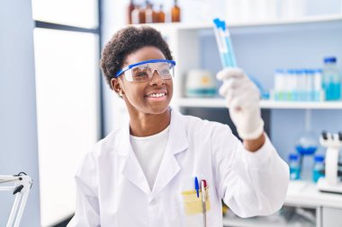 African american woman wearing scientist uniform holding test tubes at laboratory