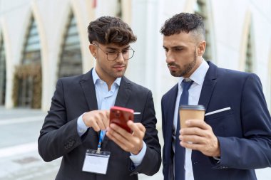Two hispanic men business workers using smartphone drinking coffee at street