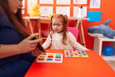 Teacher and student playing with maths puzzle game looking cards at kindergarten