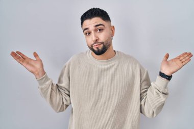 Soyutlanmış arka planda duran genç yakışıklı adam elleri ve kolları havada, kafası karışmış bir ifade takınıyor. Şüphe kavramı. 