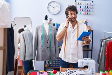 Genç İspanyol terzi akıllı telefondan konuşuyor. Giysi fabrikasında dokunmatik ped kullanıyor.