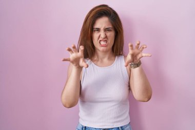 Brunette woman standing over pink background smiling funny doing claw gesture as cat, aggressive and sexy expression 